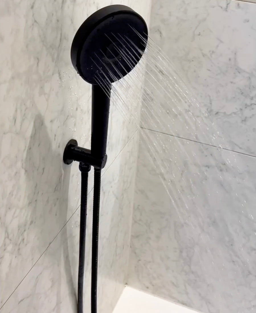 Black shower head and hose against a marble bathroom wall