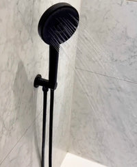 Black shower head and hose against a marble bathroom wall