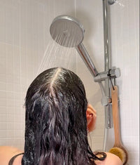 Person showering with a showerhead on a tiled bathroom wall.
