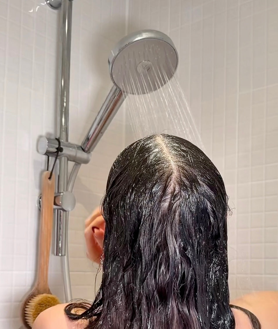 Young woman applying moisturising cream on cheek while standing in front of the mirror in bathroom.